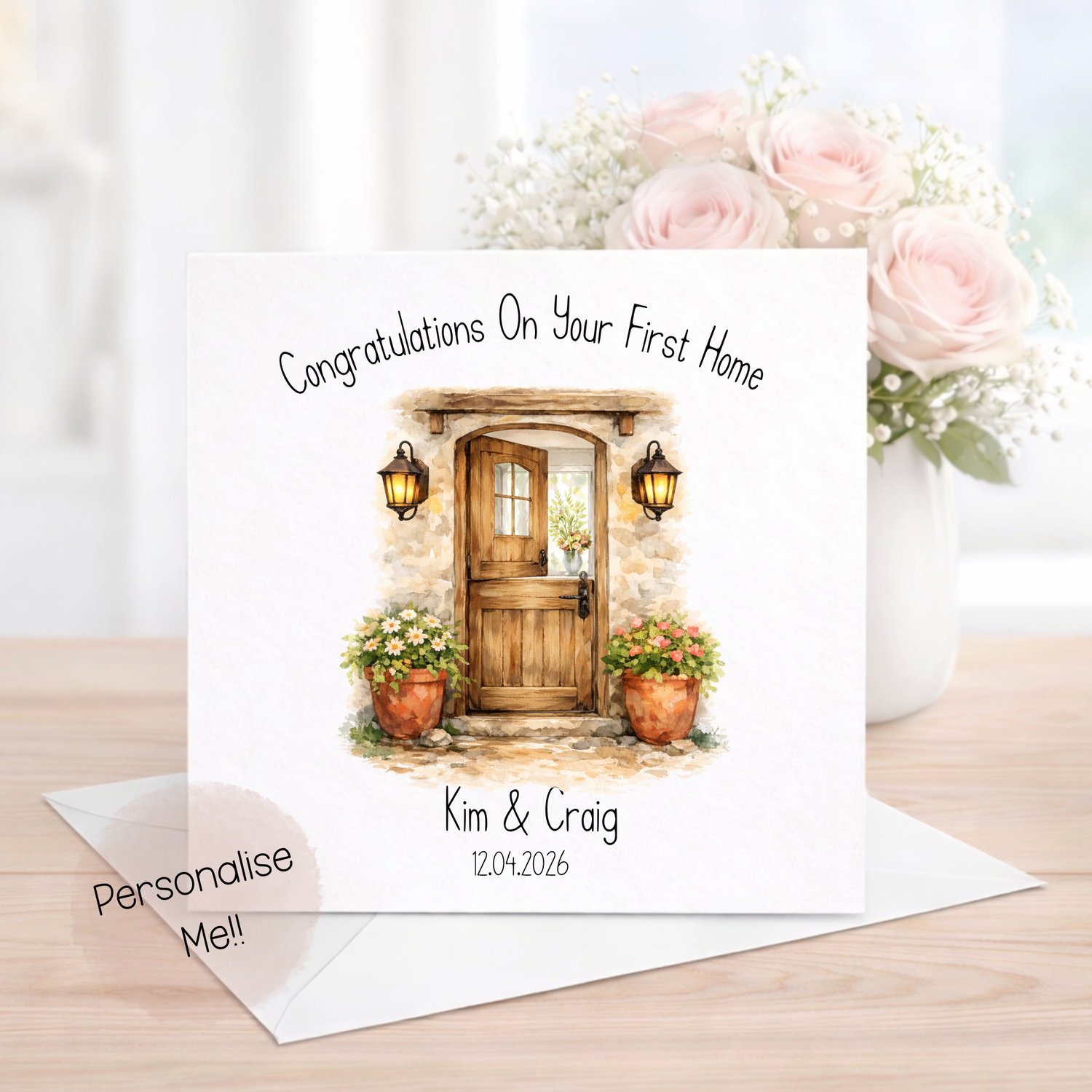 Greeting card with a house door illustration and flowers, on a wooden surface with a vase of pink roses.