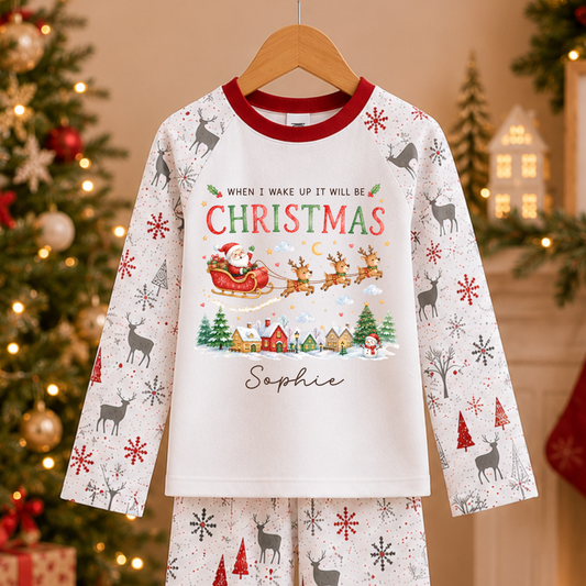 A two-piece Christmas pajama set hanging on a wooden hanger, featuring a long-sleeve top and matching pants. The pajamas are white with red trim, decorated with gray reindeer, red snowflakes, and a festive Christmas graphic on the chest.