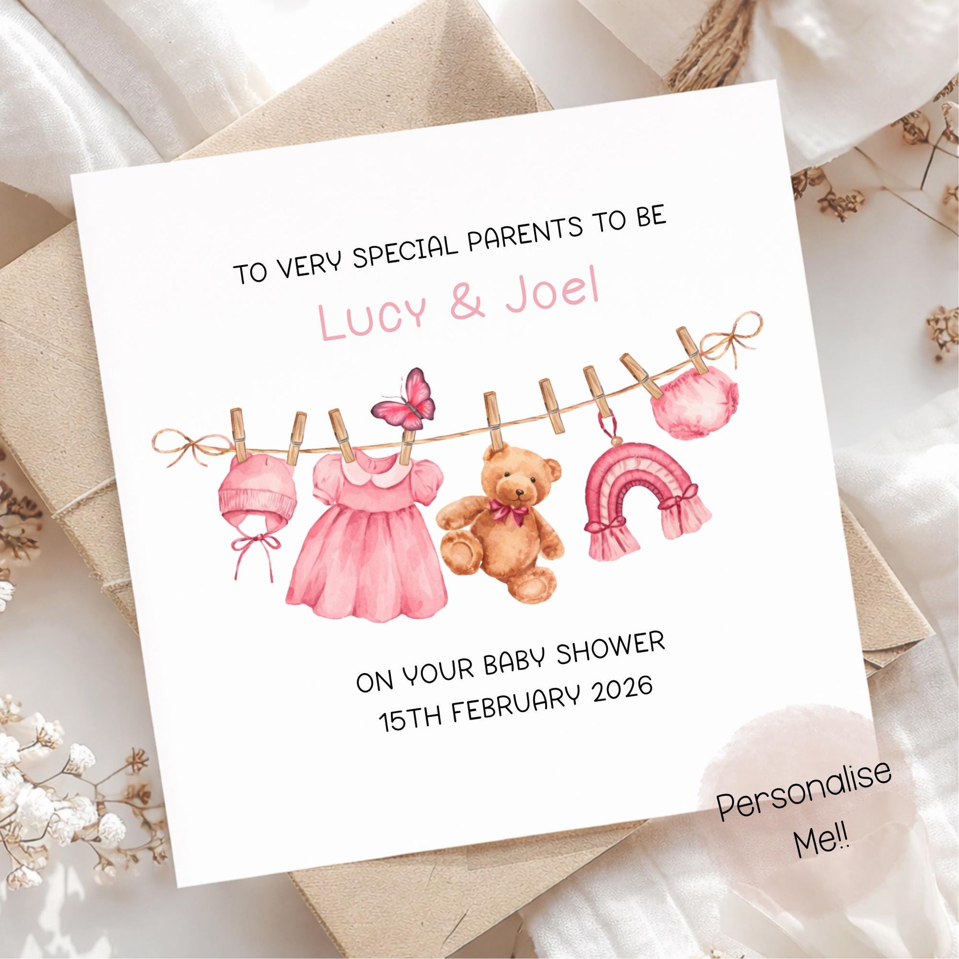 Baby shower invitation card with illustrations of a teddy bear, dress, and baby clothes on a clothesline.